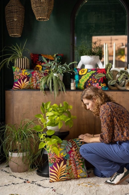 Marie Soehnlen accroupie, maniant un coussin à côté de plantes vertes