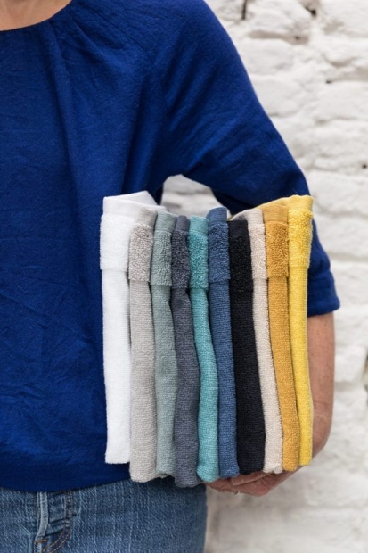 Zoom sur une femme tenant sous son bras gauche 10 serviettes de couleur pliées