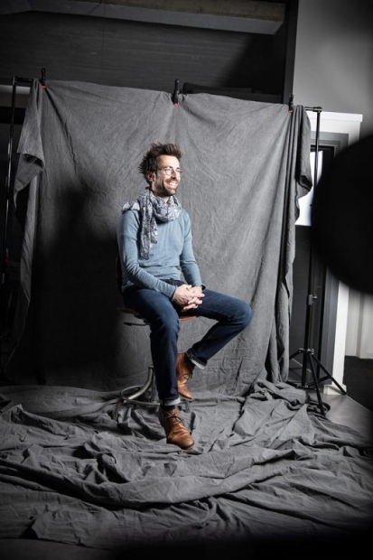 Homme souriant assis devant un drap gris dans un studio de shooting photo