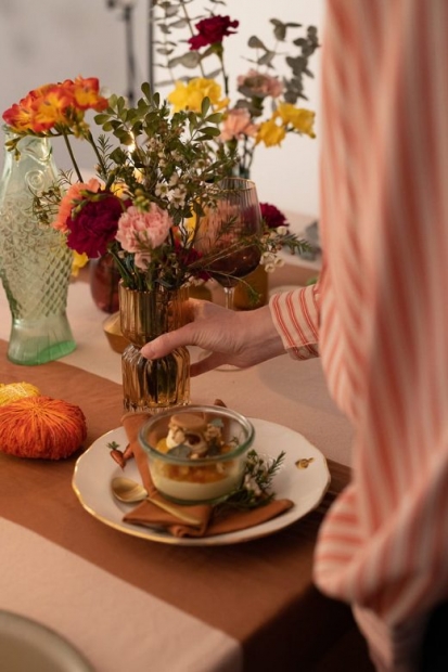 Main posant un vase rempli de fleurs sur une table servie